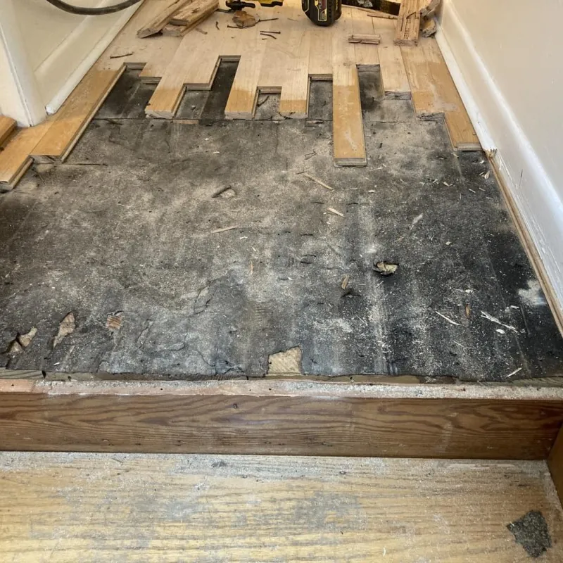 Hardwood floor opened up to the subfloor with new boards being fitted in a stagger pattern
