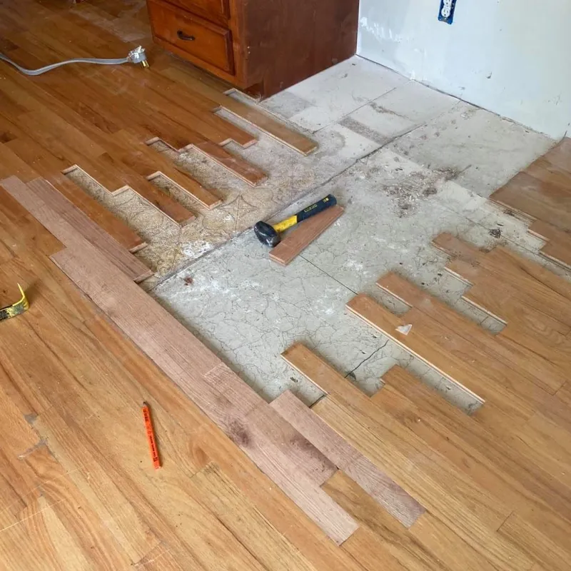 New hardwood boards being laid into an opened floor beside kitchen cabinets