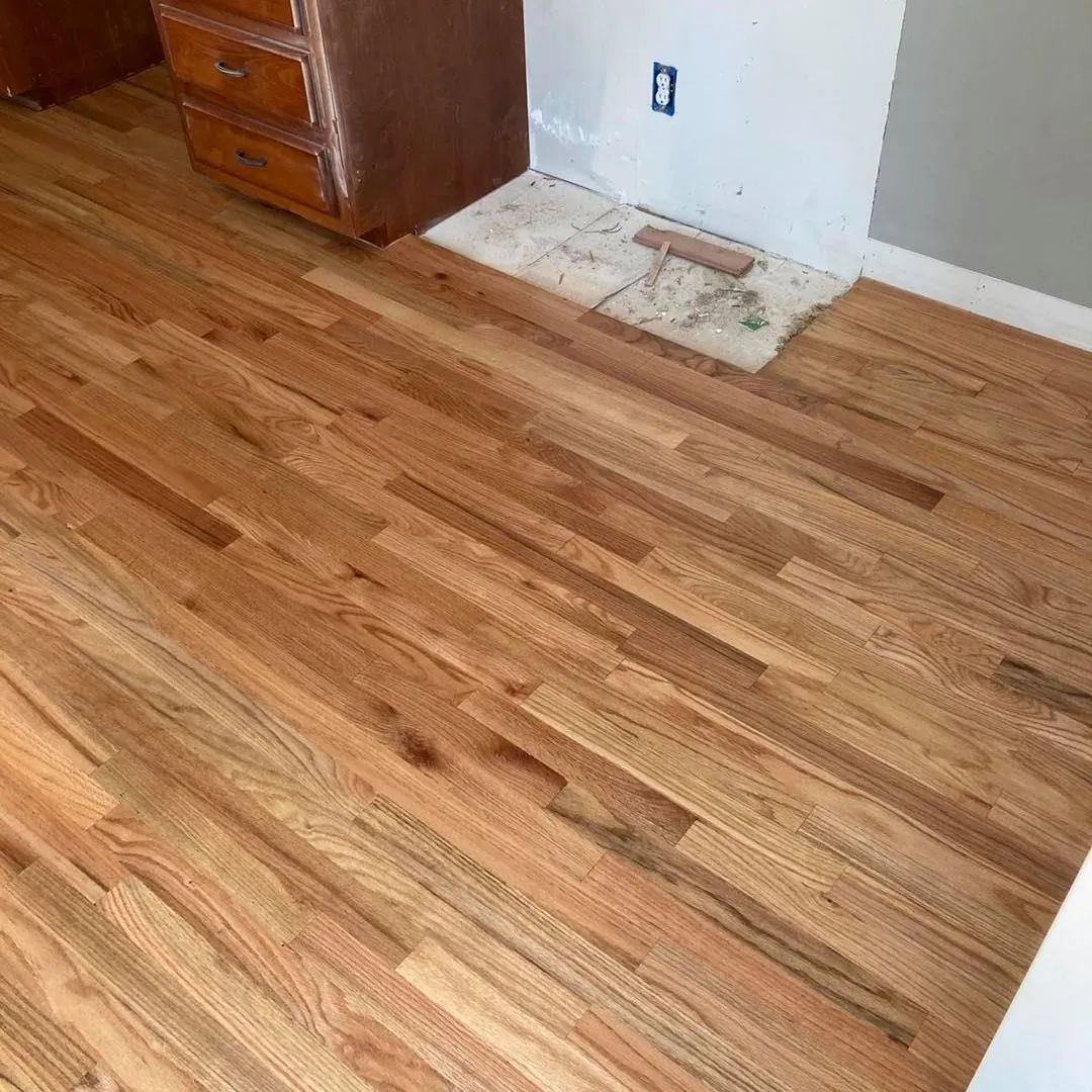 Natural oak hardwood floor with a patch of subfloor showing beside a dresser, ready for new boards